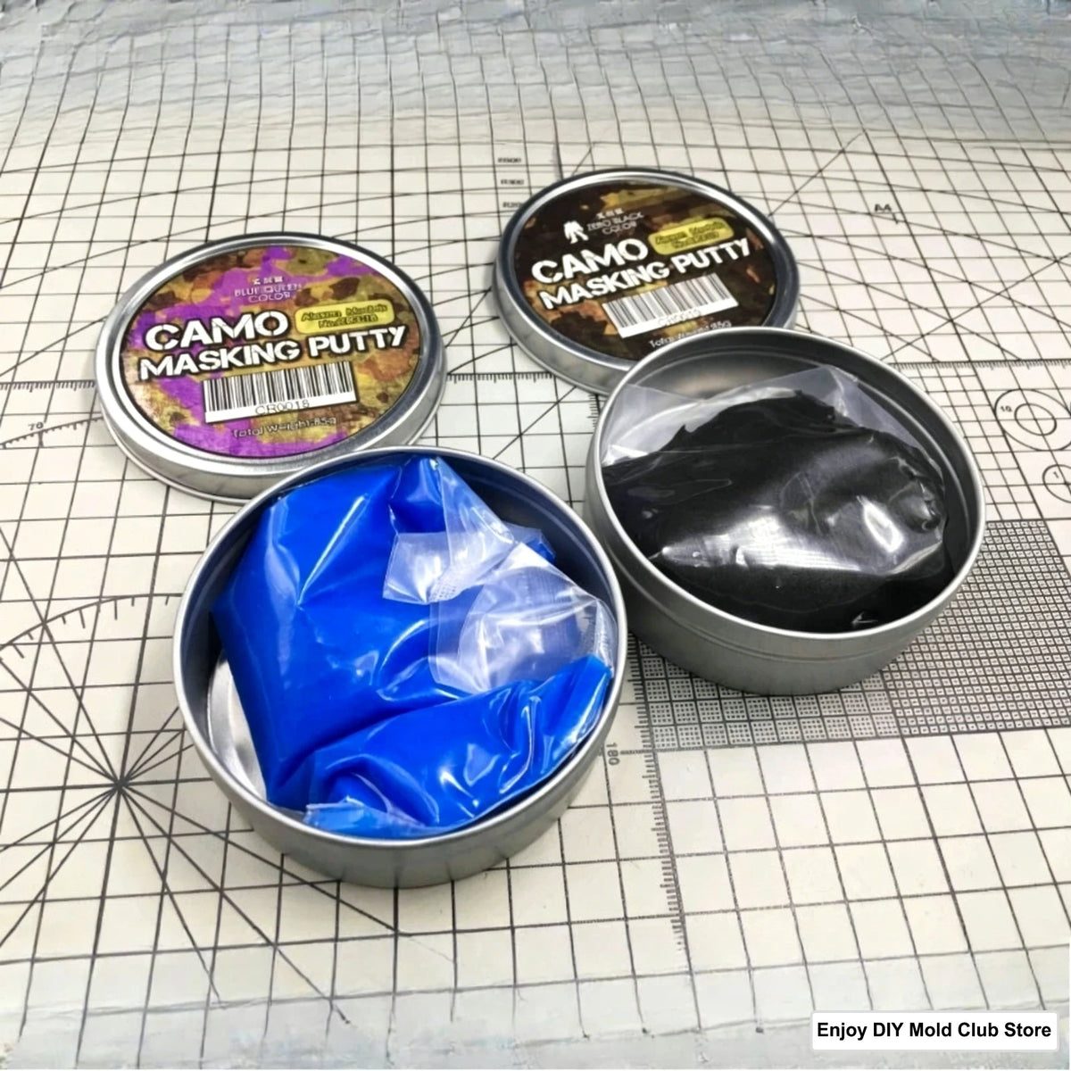 A collection of Camo Masking Putty tins and a blue putty in a metal container on a grid surface.