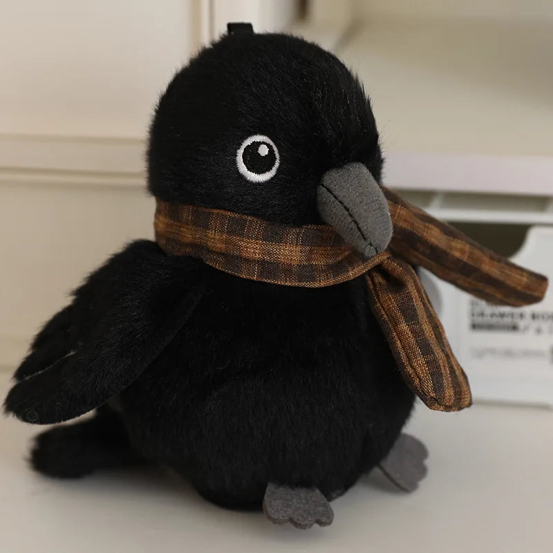 A black cartoon bird plush with a brown plaid scarf resting on a white surface.