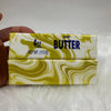 A rectangular butter stick with white and yellow marbled design is shown next to a hand.