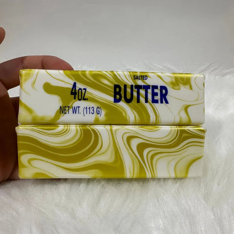 A rectangular butter stick with white and yellow marbled design is shown next to a hand.