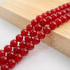 A string of round, polished natural red carnelian beads laid on a light wooden surface.