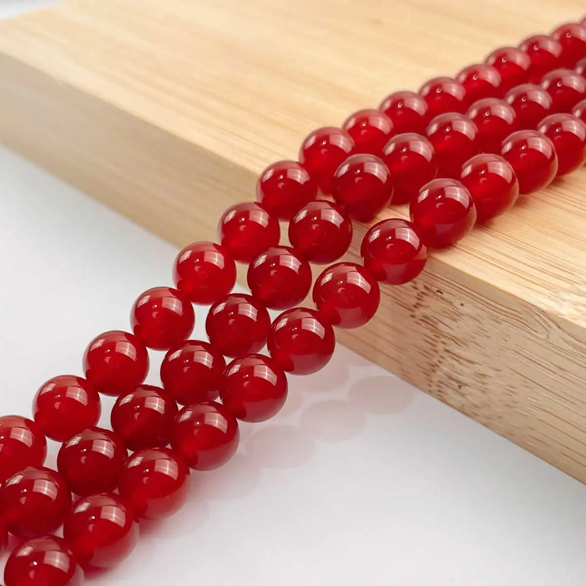 A string of round, polished natural red carnelian beads laid on a light wooden surface.