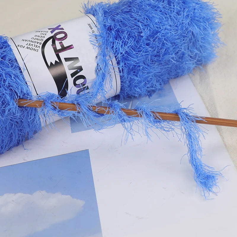 A roll of bright blue chunky faux fur yarn with a wooden knitting needle resting on a white surface.