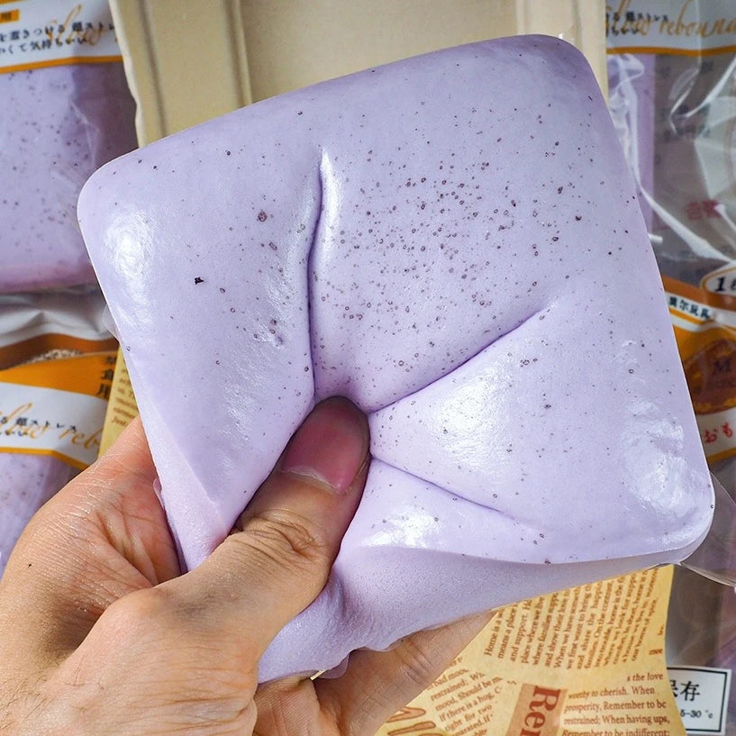 A hand holds a purple Slow-Rise Toast Squishy stress relief toy, showing its squishy texture and shape.