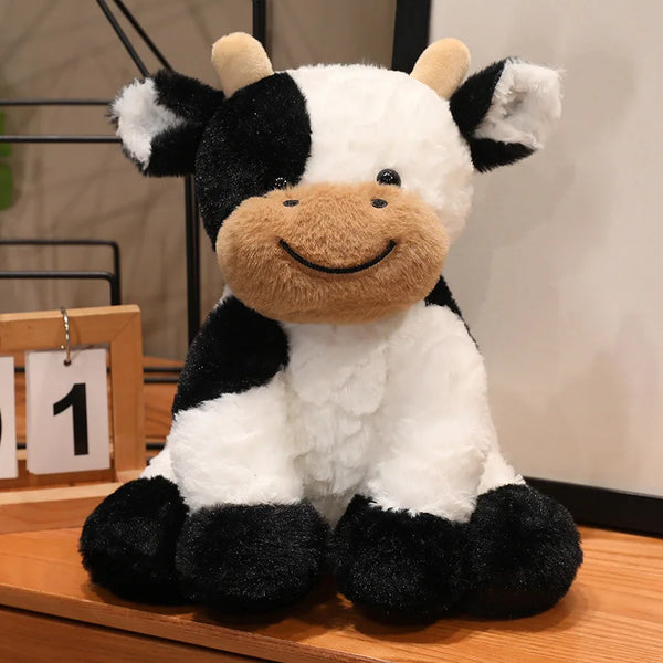 A plush cow stuffed animal toy with black and white markings sitting on a wooden surface.