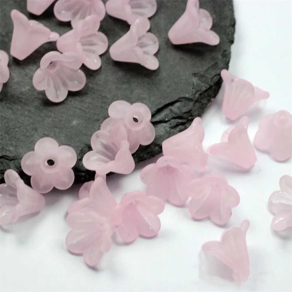Pink frosted acrylic flower beads scattered on a dark slate surface