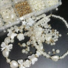 A collection of white and gold pearl beads, including various shapes like hearts, flowers, and butterflies, displayed in clea