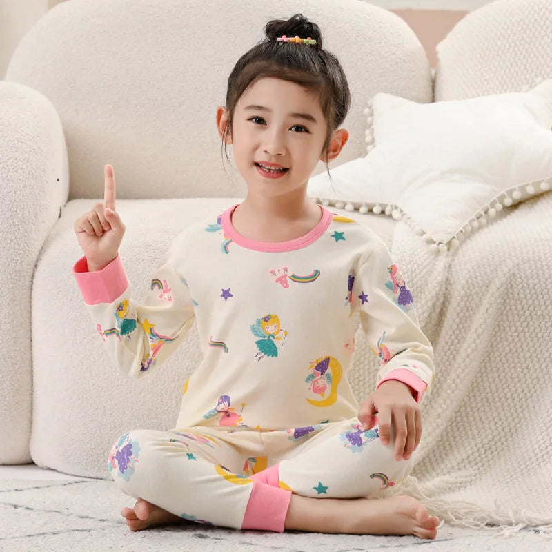 A smiling young girl wearing a cream-colored cotton pajama set with a colorful astronaut print.