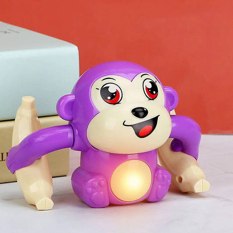 Un jouet singe électrique violet avec de grands yeux et un ventre lumineux, assis sur une surface blanche.