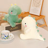 A soft green dinosaur plush toy sitting next to a white dinosaur plush toy on a table.