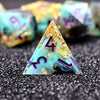 A single triangular resin die with purple numbers is placed on a dark surface next to other dice.