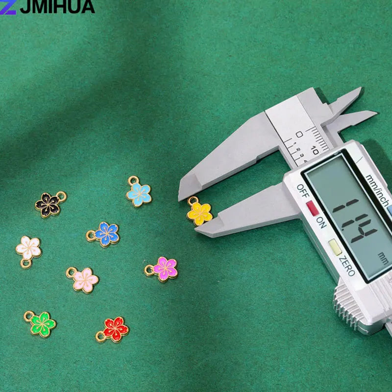 A silver craft knife is shown next to 15 small enamel flower and cherry charms on a green surface.