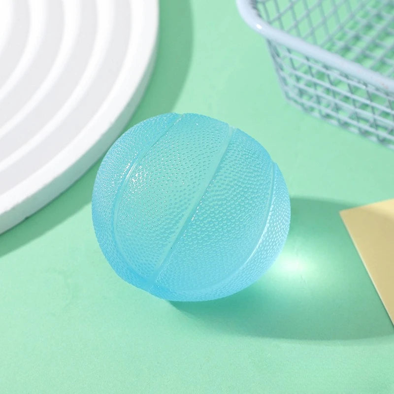 A round, light blue squishy fidget toy with a textured surface is shown on a green surface next to a white plate and a mesh b