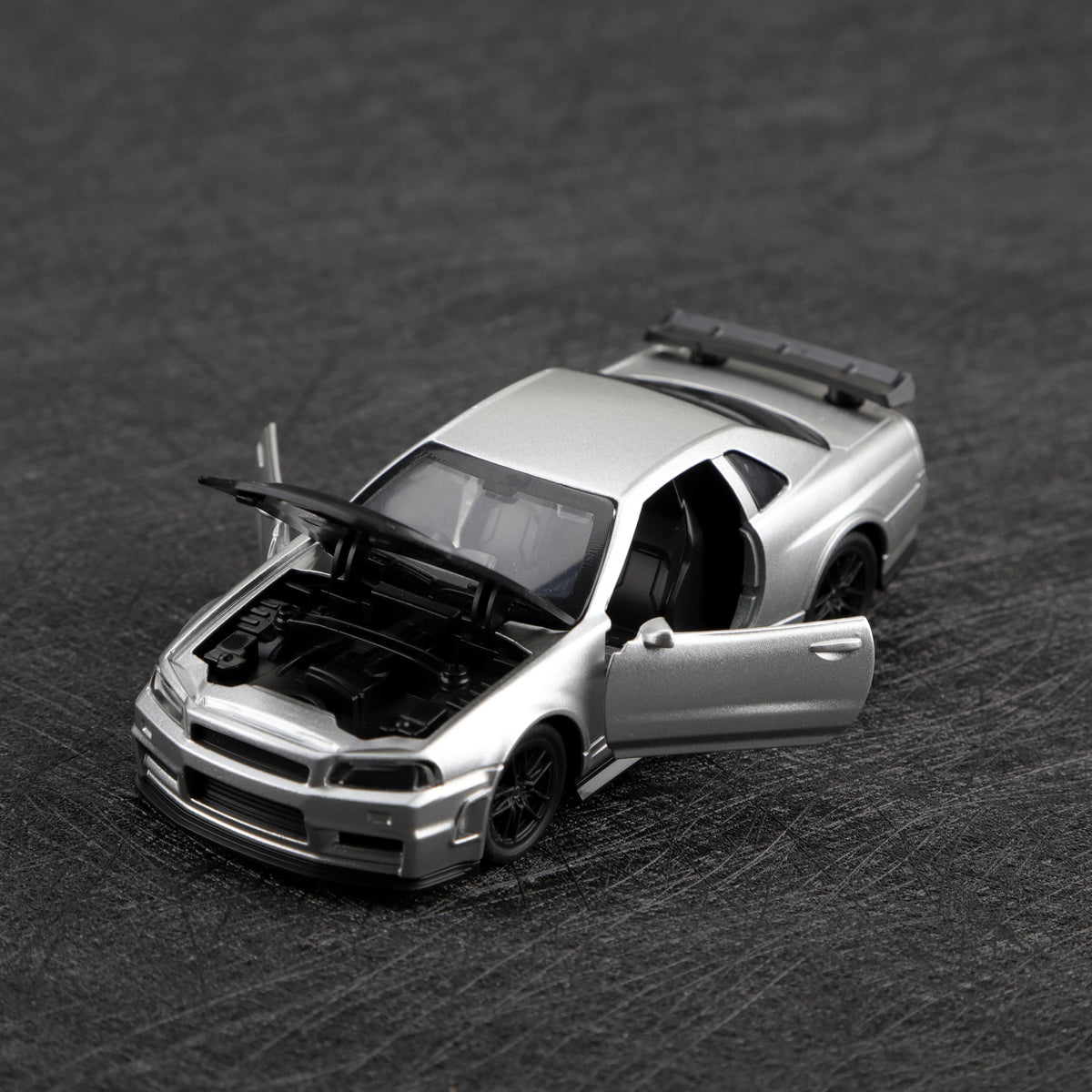 A silver die-cast sports car model with a pull-back feature is shown on a dark surface.