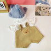 A fluffy blue teddy bear plush wearing a light-colored outfit is displayed next to a wooden frame.
