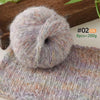 A ball of light gray and purple alpaca blend yarn resting on a knitted item.