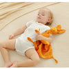 A baby lies on a cream blanket, gently holding an orange fabric toy.