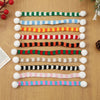 A set of mini knit Christmas hats and scarves featuring various striped colors like green, white, blue, red, and yellow.