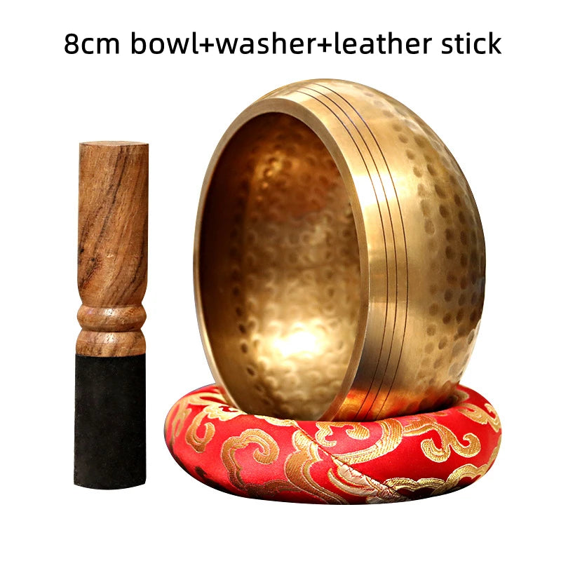A handmade copper singing bowl with a washer and leather stick resting on a red fabric base.
