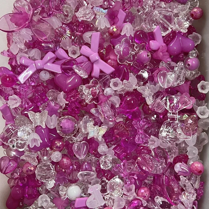 A close-up view of a mixed pack of pink and purple acrylic bow and flower beads for jewelry making.
