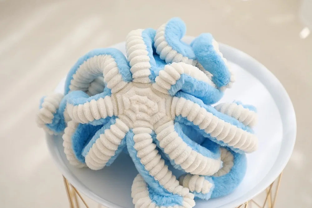 Adorable octopus plush toy with blue and white fuzzy tentacles resting on a white plate.