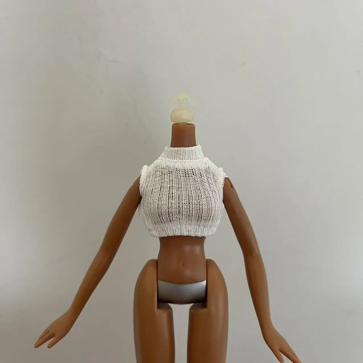 A brown doll with a white knitted top and a blonde hairpiece, shown from the back.