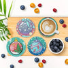 An arrangement of colorful fruits and a coffee cup displayed on a wooden board with diamond painting coasters.