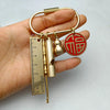 A brass keychain featuring a measuring ruler, a cylindrical object, and a round red emblem on a gold ring.