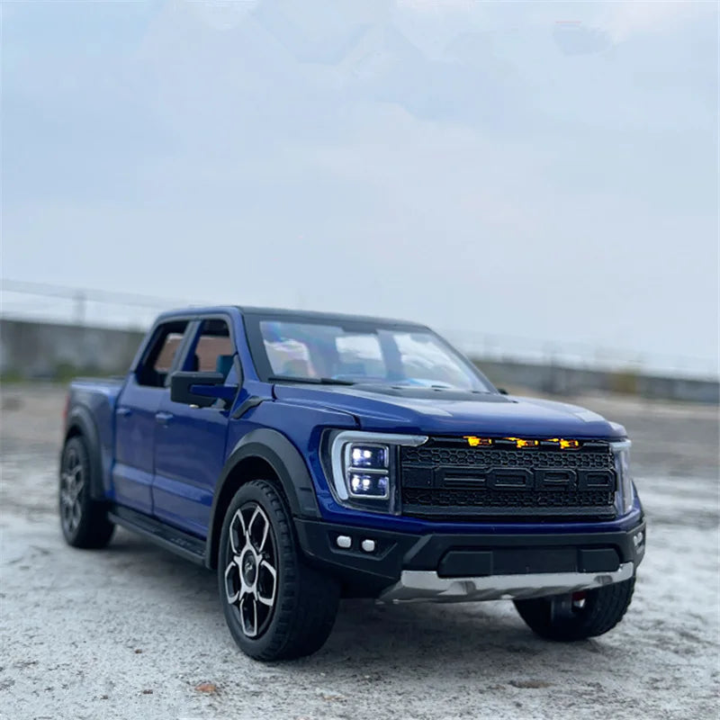 A blue 1:20 scale Ford Raptor F150 diecast model truck with lights parked on a gray outdoor surface.