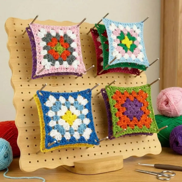 A wooden crochet blocking board set with pins holds several colorful knitted or crocheted fabric squares.
