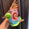 A hand holds a pink and blue plush keychain shaped like a swirling monster, featuring a green head.