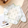 A white and green patterned waterproof long sleeve feeding bib for babies lying on a beige textured cloth.