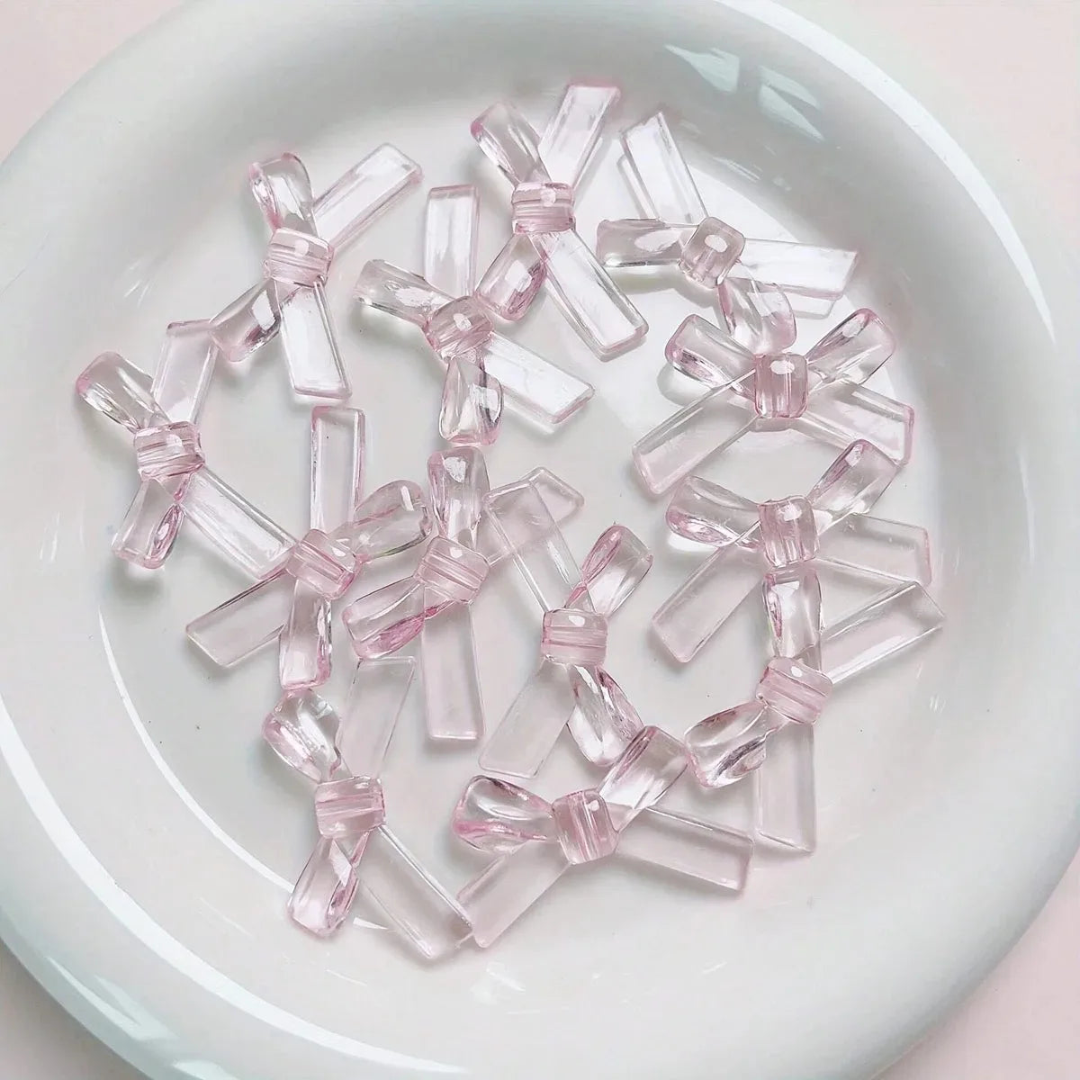 A collection of clear pink acrylic bow tie beads arranged on a white plate.