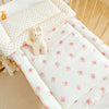 A white fleece beanie blanket with pink bunny patterns is displayed on a wooden crib railing.