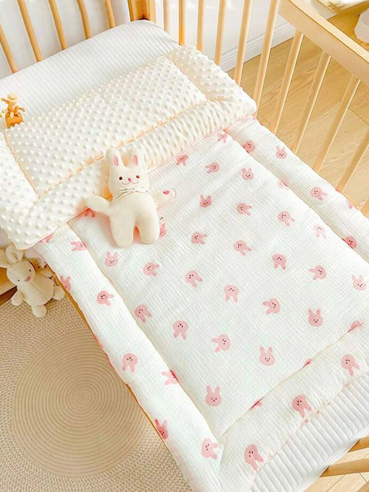 A white fleece beanie blanket with pink bunny patterns is displayed on a wooden crib railing.