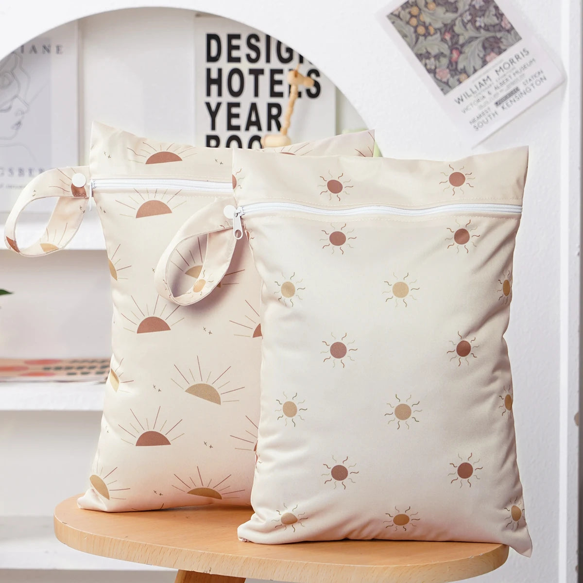 A set of two beige reusable waterproof baby wet bags with a sun pattern displayed on a white shelf.