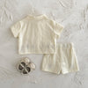 A cream-colored baby cotton shirt and shorts set with a subtle flower pattern laid on a white surface.