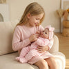 A young girl is holding a lifelike soft body baby doll in a pink knitted outfit.