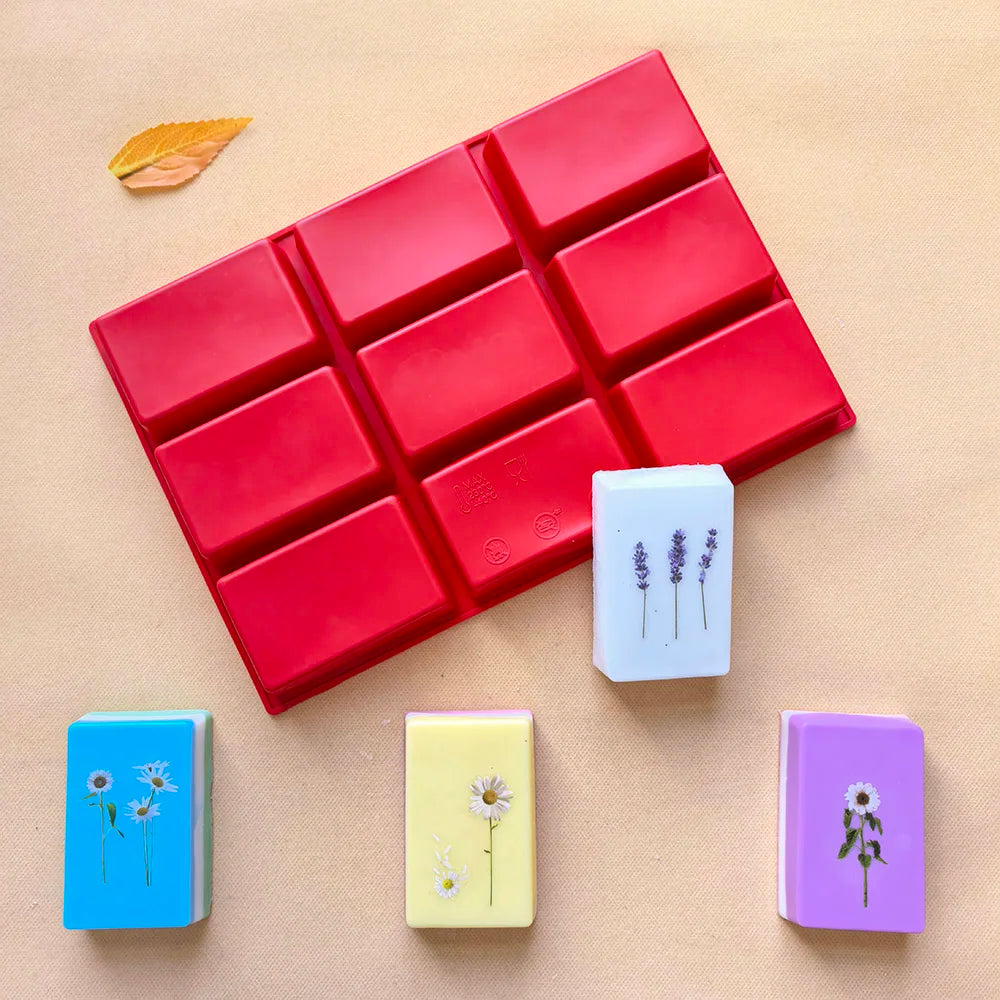 A red silicone mold with nine cavities is shown alongside several small blocks of soap or craft material in various colors.