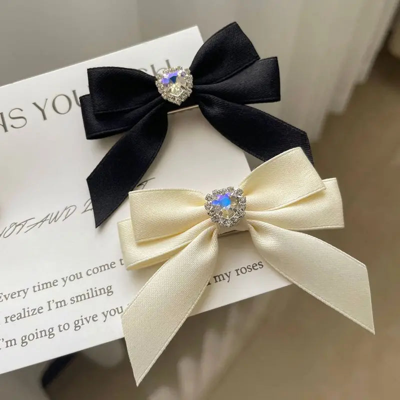 A black satin bow with a rhinestone heart embellishment used as a hair clip.