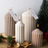 Three tall, cylindrical silicone candles with a striped design displayed next to pine greenery and natural wood.