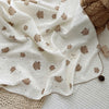 A white muslin swaddle blanket with a floral print featuring small brown animal shapes is draped on a light surface.