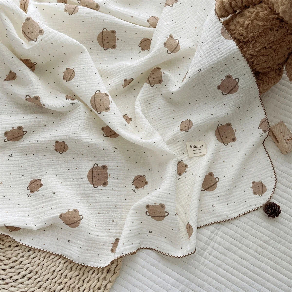 A white muslin swaddle blanket with a floral print featuring small brown animal shapes is draped on a light surface.