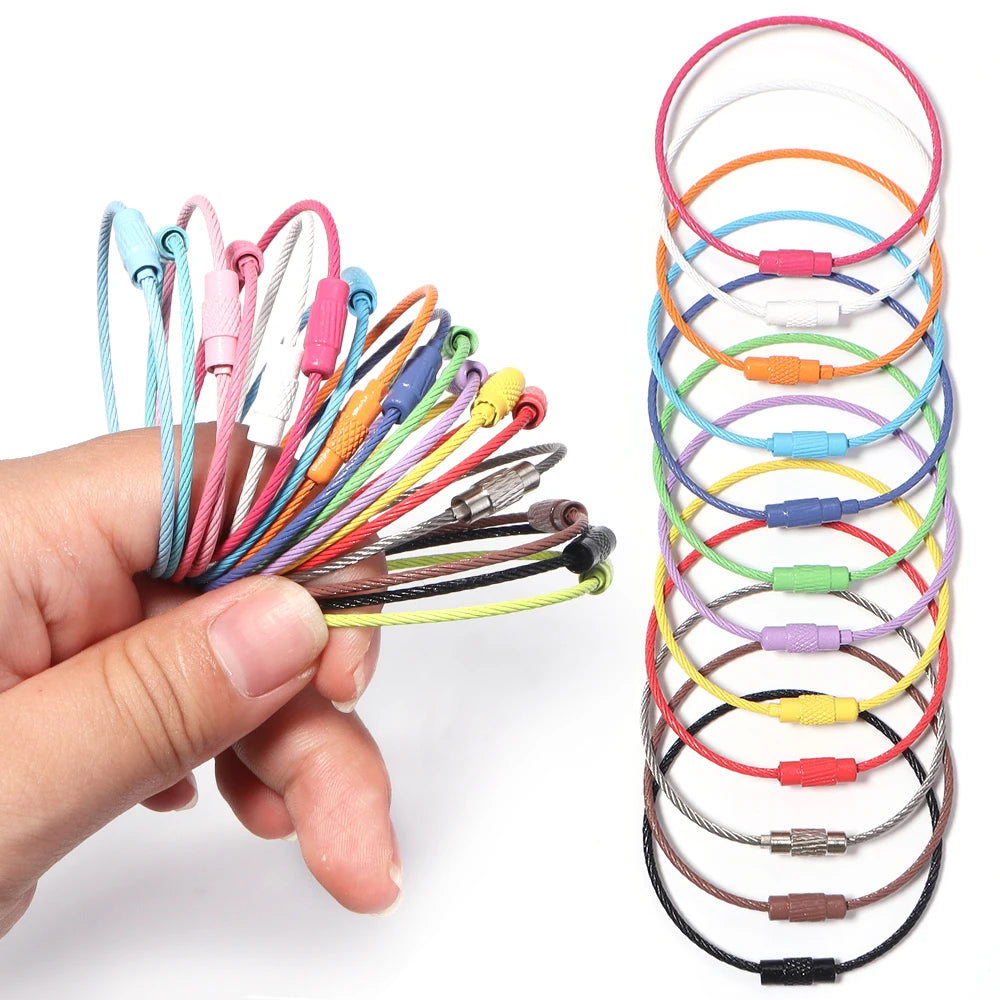 A hand holds a collection of 10 stainless steel wire keychain rings in various colors, arranged in a spiral pattern.