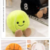 A yellow plush doll shaped like a sports ball with stitched features and brown hands, displayed next to an orange plush ball.