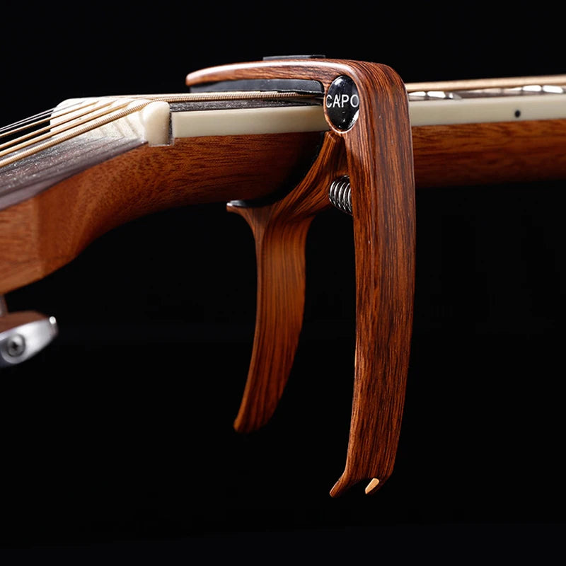A close-up view of a professional metal guitar capo with a pick holder, made of dark wood and metal.
