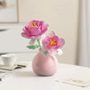A pink ceramic vase holds a vibrant pink and orange artificial flower, part of a floral bouquet building block set.
