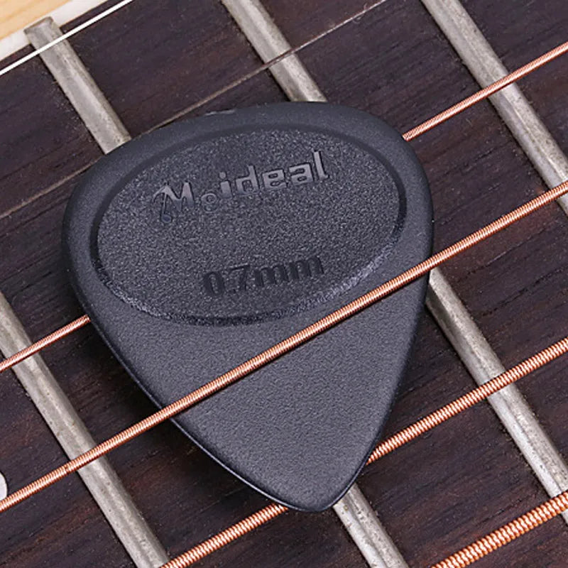 A black non-slip nylon guitar pick labeled Mideal resting on a wooden fretboard.