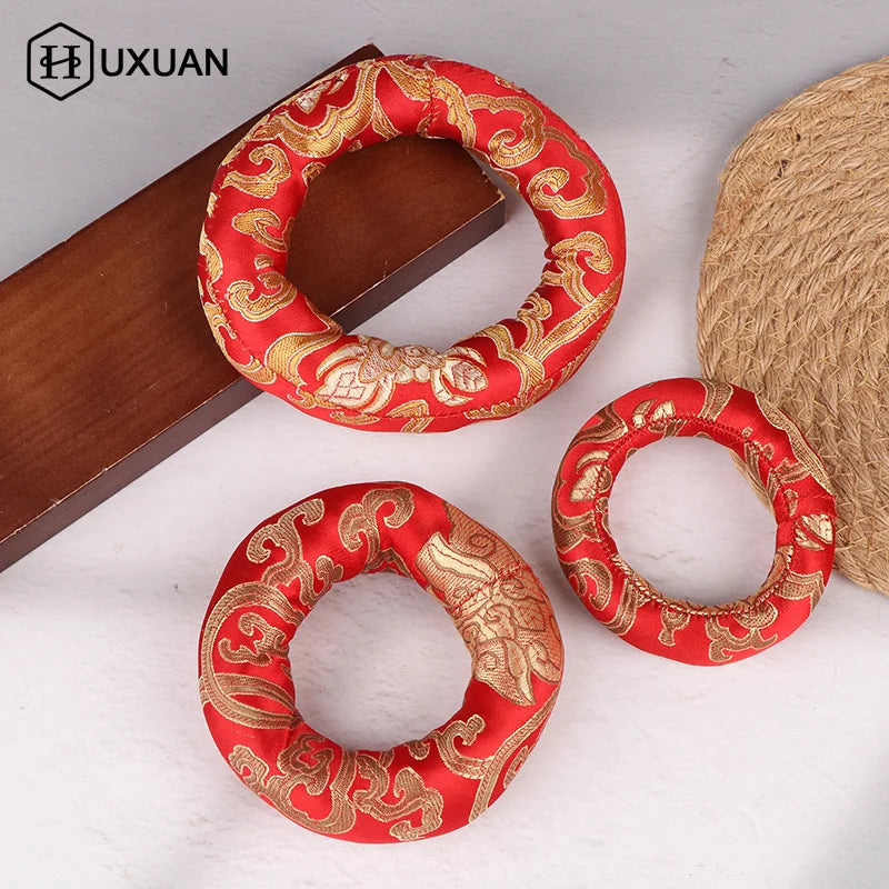 A handmade red singing bowl cushion with gold embroidery is displayed on a wooden surface.