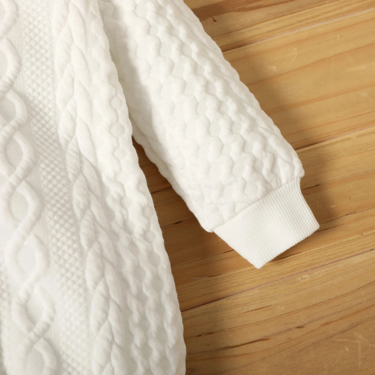 A white quilted hooded baby romper lying on a wooden surface.
